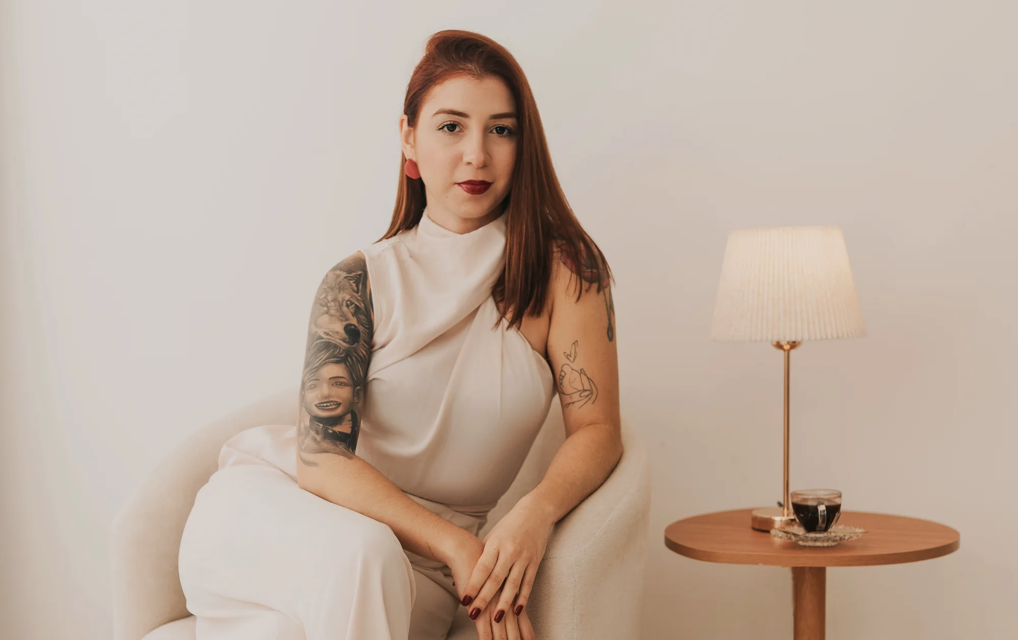 Fernanda Smanio sentada em uma poltrona clara, ao lado de um abajur